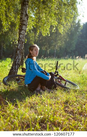 Young cyclist enjoying relaxation in spring in the morning park sitting in the birch trunk