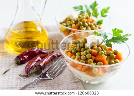 Vegetarian salad with canned peas and boiled vegetables. Hot peppers, bottle vegetable oil and fork on napkin fabric