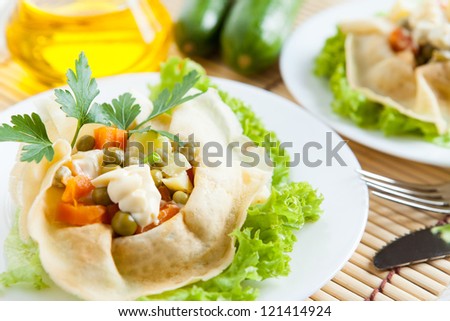 Salad with cooked vegetables, mayo and greens wrapped in a pancakes on a plate. Salad with cooked vegetables, mayo and greens wrapped in a pancake on a plate. Bottle oil and cucumber in the background