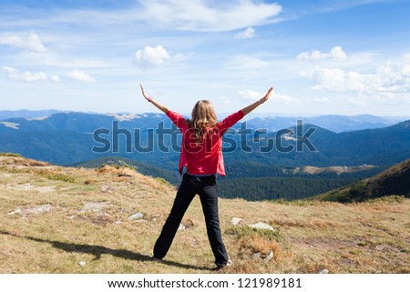 Hiker woman on a peak mountain with raised hands embracing vitality freedom. Position back to us
