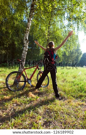 Excited young cyclist standing in a spring park with hands outstretched. Sunny outdoor