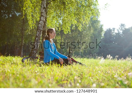 Girl cyclist enjoying relaxation in spring park sitting in the fresh green grass