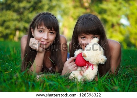 Portrait beautiful young twins sisters relaxation lying on the green grass in a sunny summer green park. Outdoor