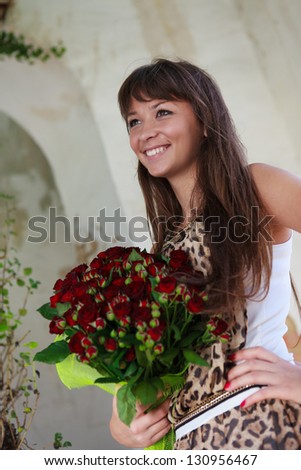 Beautiful smiling woman with a bouquet of red roses. Outdoor