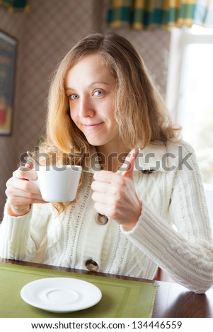 Happy young woman with a cup of coffee in hand showing thumb up sign. Coffee-break