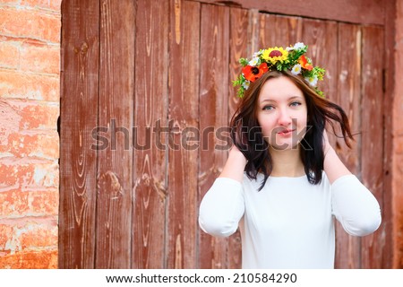 Closeup portrait of beautiful young woman with flower wreath on her head near the wooden door. Beauty concept