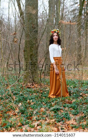 Young girl with flower wreath on her head and orange skirt in the autumn forest