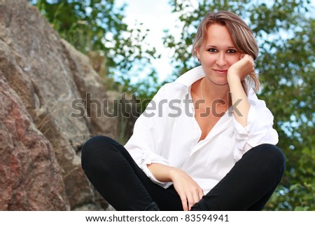 A beautiful young woman sitting cross-legged among the stones and propped a hand face