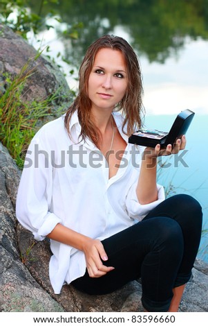 A beautiful woman with makeup kits in hand sitting on a stones by the coast river