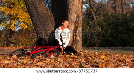 Relaxes woman cyclist with bike sits among fallen leaves leaning against a tree autumn morning in nature illuminated by the rays of the rising sun and enjoy recreation
