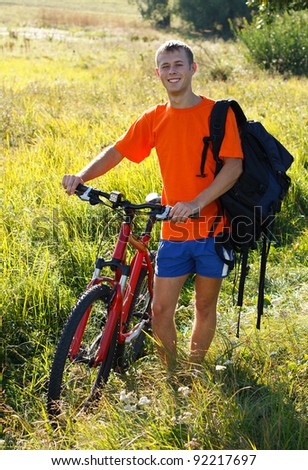 Happy man cyclist with a bicycle and a backpack on his shoulder against a background of green nature