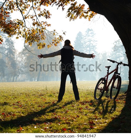 Excited woman cyclist standing in a park with hands outstretched embracing vitality freedom. Outdoor