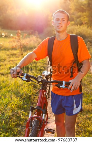Happy man cyclist with bicycle walk a backpack behind shoulders illuminated by the rays of summer sun