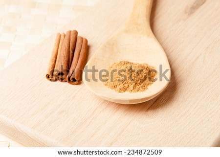 Three cinnamon sticks on a plank and cinnamon powder on a wooden spoon