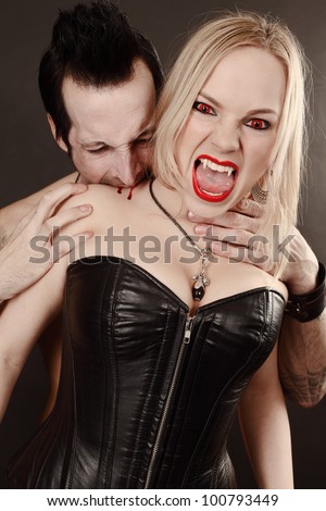 Photo of a female vampire with mouth open and fangs showing being bitten by male vampire.  Desaturated to create pale skin.