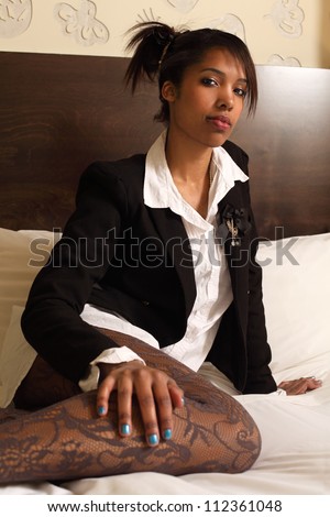 Photo of a gorgeous woman of African descent sitting on her bed looking at the camera.