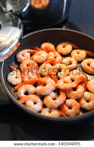Photo of shrimp being fried in butter on a black frying pan. Shallow depth of field with focus across the middle.