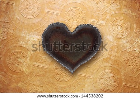Photo of a metal heart on top of a vintage tattered wallpaper background.