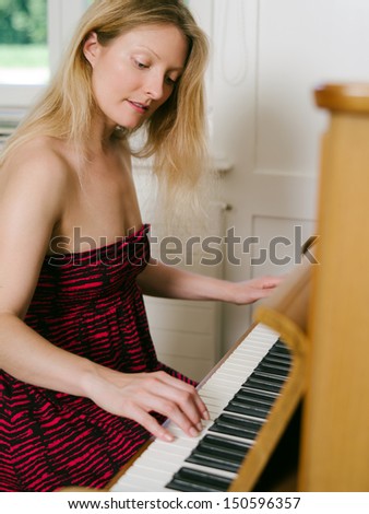 Photo of a happy blond female in her early thirties playing the piano at home.