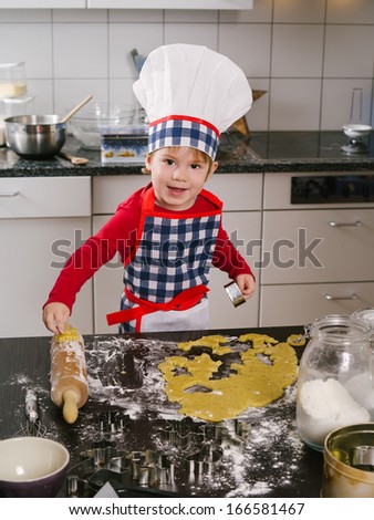 Photo of an adorable boy in a chef hat and apron making cookies in the kitchen.