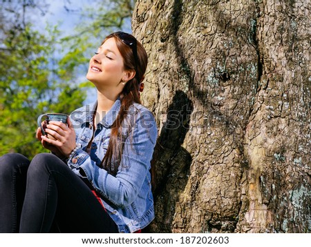 Photo of a beautiful young woman enjoying the warmth of the sun in early spring while she drinks her coffee.