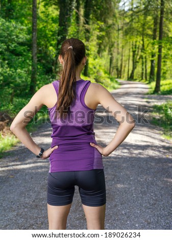 Photo of a young woman looking down the gravel path through a forest before she starts her exercise.