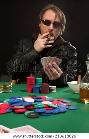 Photo of a man playing poker while wearing sunglasses and smoking a cigar.