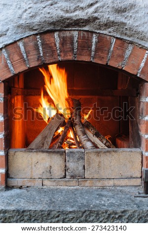 Photo of an outdoor brick fireplace with a fire blazing inside.
