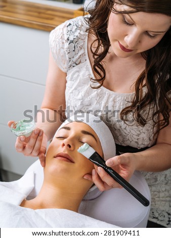 Photo of a young beautiful girl receiving a green facial mask in spa beauty salon.