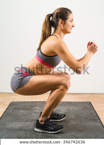 Photo of a young woman exercising and doing a isometric squat on a black floor mat.