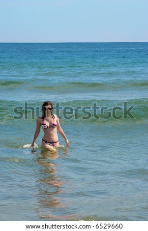 A bikini clad female emerging from the waves after a swim.