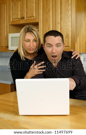 A loving couple, searching the internet on their laptop in their kitchen, and discovering something shocking.