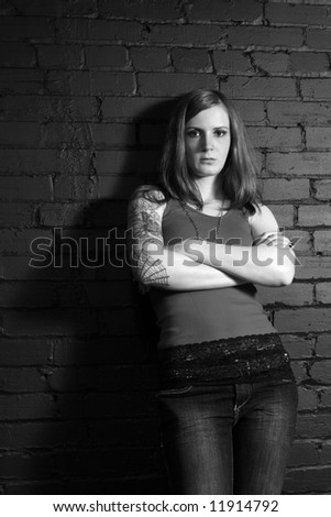stock photo : A young female with full arm tattoo leaning up against a black brick