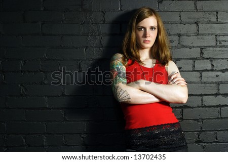 stock photo A young female with full arm tattoo leaning up against a black 