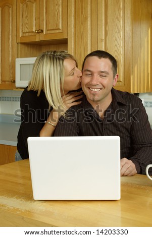 A loving couple, searching the internet on their laptop in their kitchen.
