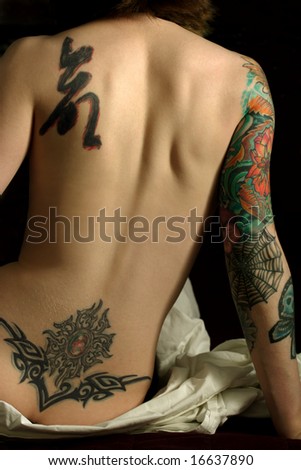  photo : A young slim women with arm and back tattoos sitting on the bed