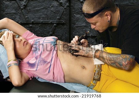  photo : A tattoo artist applying his craft onto the abdomen of a female.