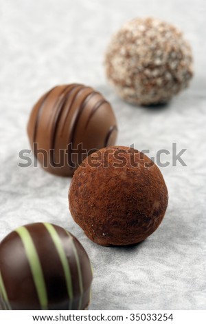 A small assortment of chocolate truffles and pralines on paper.  Very Shallow depth of field, focusing on middle truffle.
