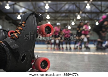 An abstract image of the roller-skates of a fallen skater as her teammates in the background continue to skate around the track of the roller derby.