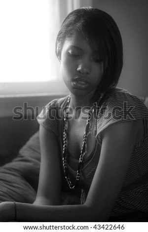 A beautiful female sitting by a window in deep thought.