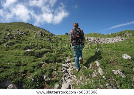 Photo of an active female with backpack hiking up a mountain trail. Slight motion blur on hiker.