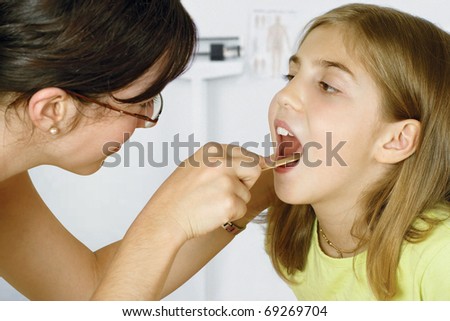 Doctor in her office checking the throat of a young patient.