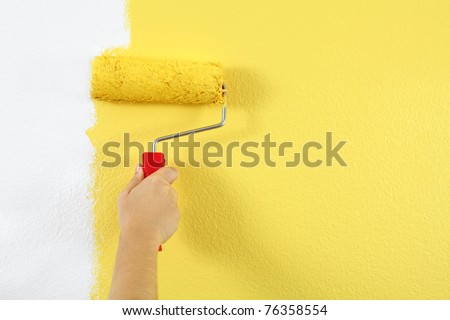 Photo of a female painting a wall with a roller and yellow paint.
