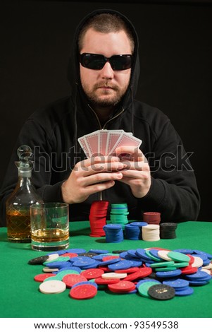 Photo of a hooded man playing poker while wearing sunglasses. Playing cards have been altered to be generic.