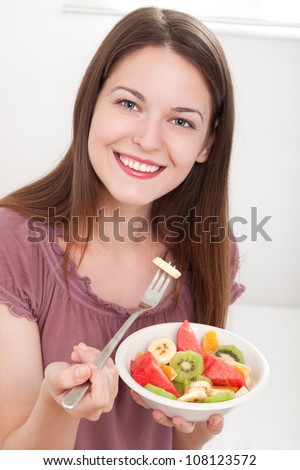 Beautiful young woman smiling and eating fruit salad, on white background