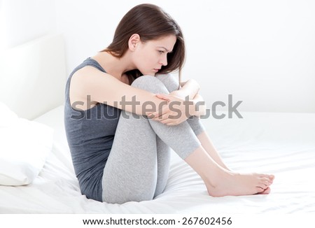 Sad looking young woman sitting on bed, on white background