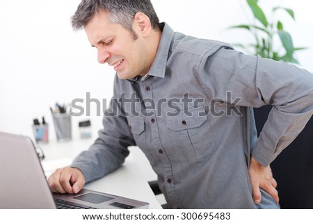 Image of a young man having a back pain while sitting at the working desk