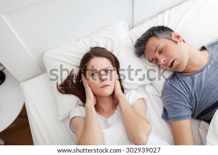 Woman covering ears, annoyed by the snoring of her husband
