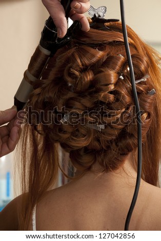 Close up of stylist\'s hand using curling iron for hair curls