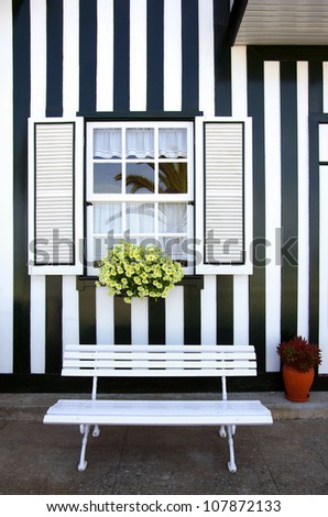 White bench and window of a typical striped house in Costa Nova, Portugal.